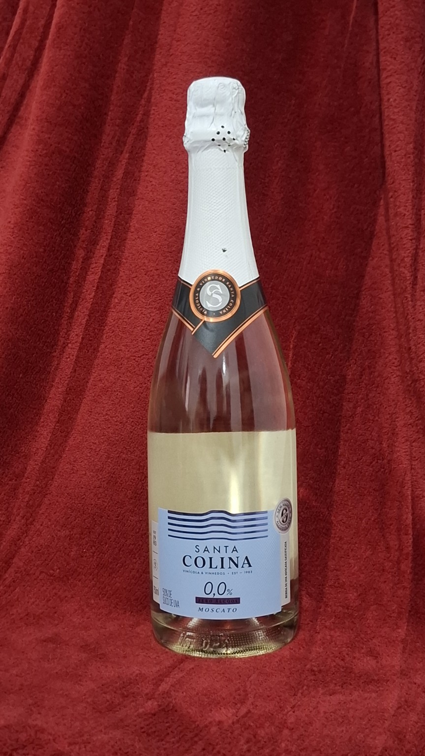 Garrafa de Santa Colina 0,0% Moscato em fundo vermelho